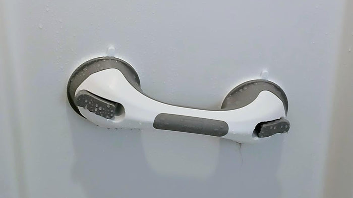 A white and gray bathroom grab handle mounted on a white door, with water droplets visible on the surface.